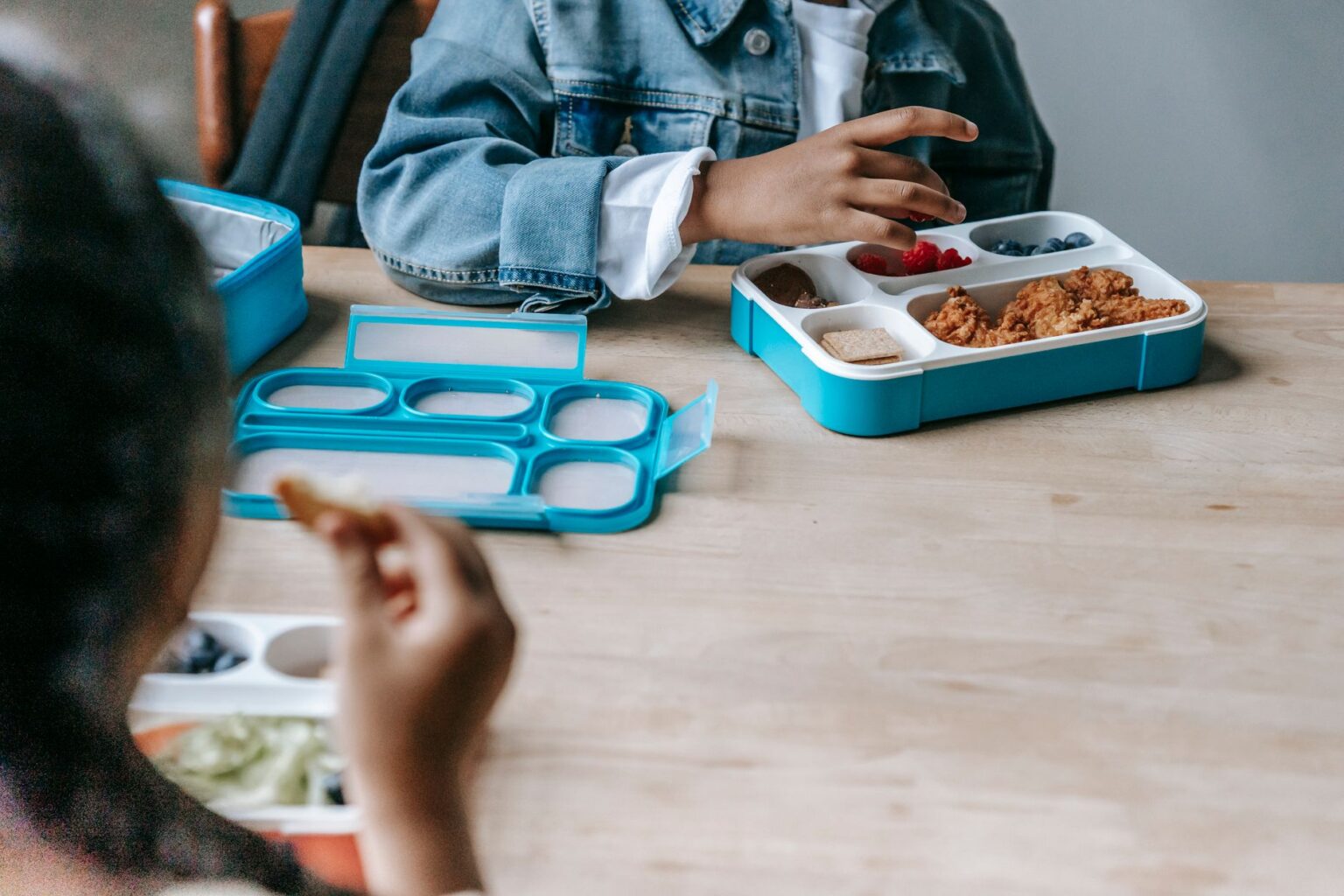 Children eating lunch from food boxes at a shared table